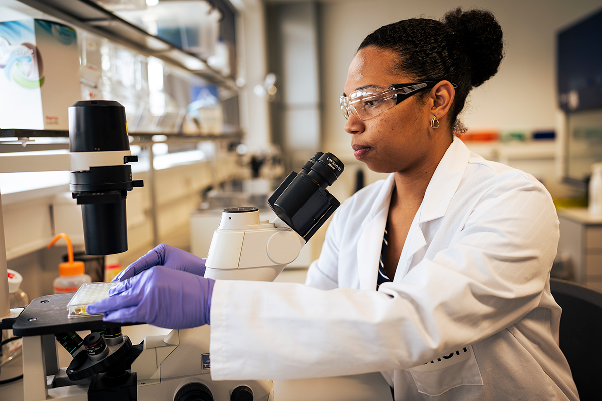 Female Sanofi team member using a microscope in a lab